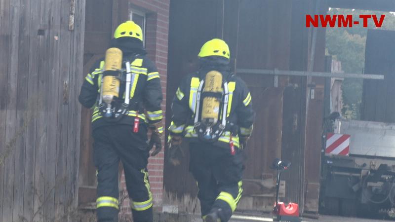 Holzlager brennt in Unterstand direkt an einer Halle – Rauch zieht durch das gesamte Gebäude – Feuerwehrkräfte löschen das Feuer und kontrollieren die Halle